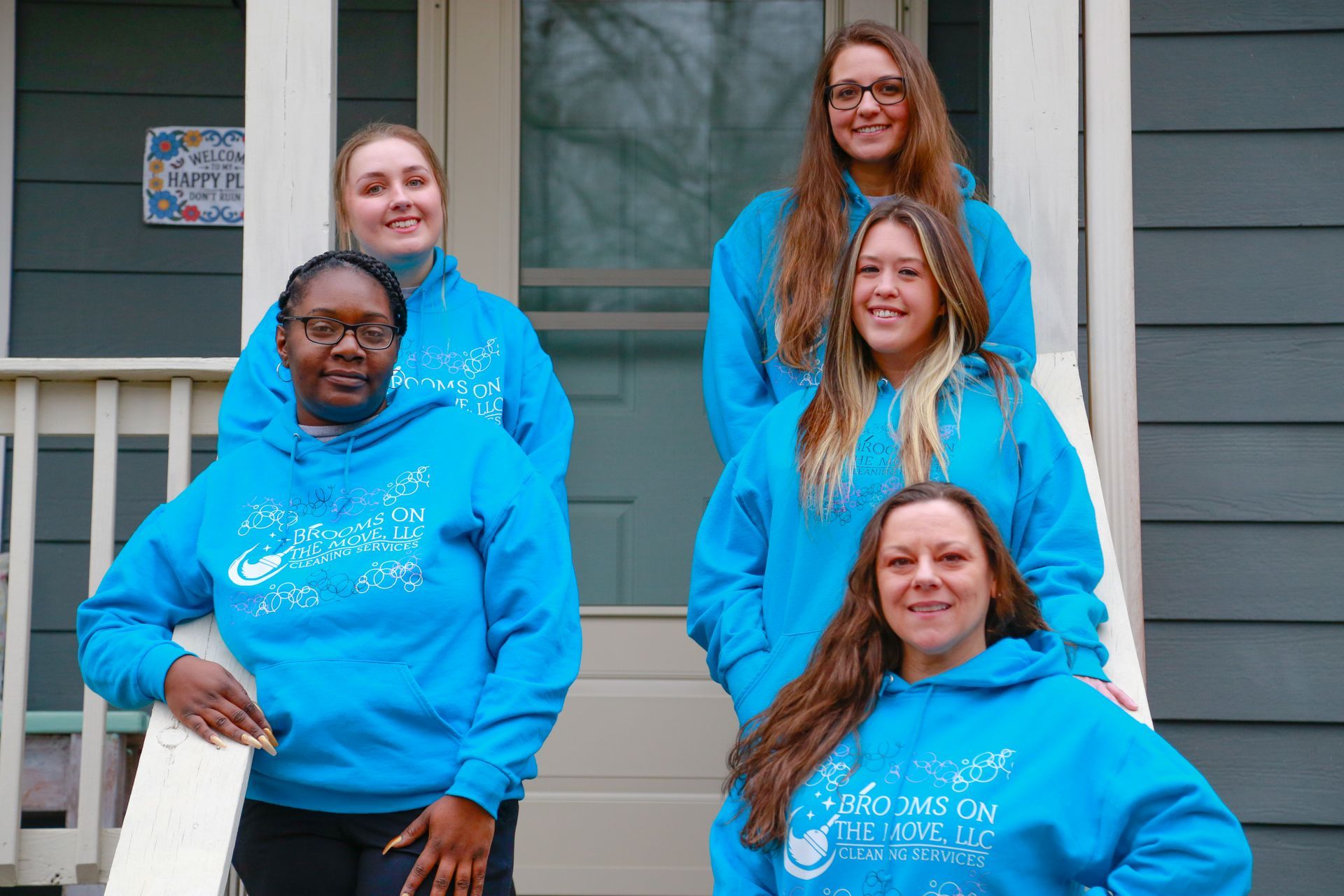 Five people in matching blue hoodies pose on a porch.