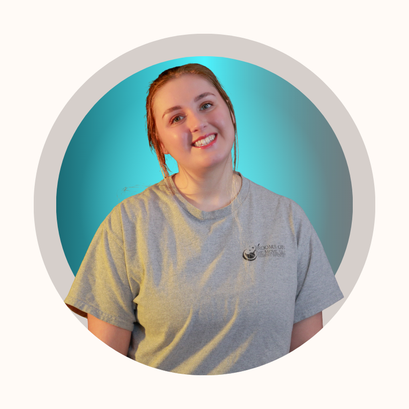 Woman with red hair smiling, wearing a gray t-shirt, against a teal and white background.