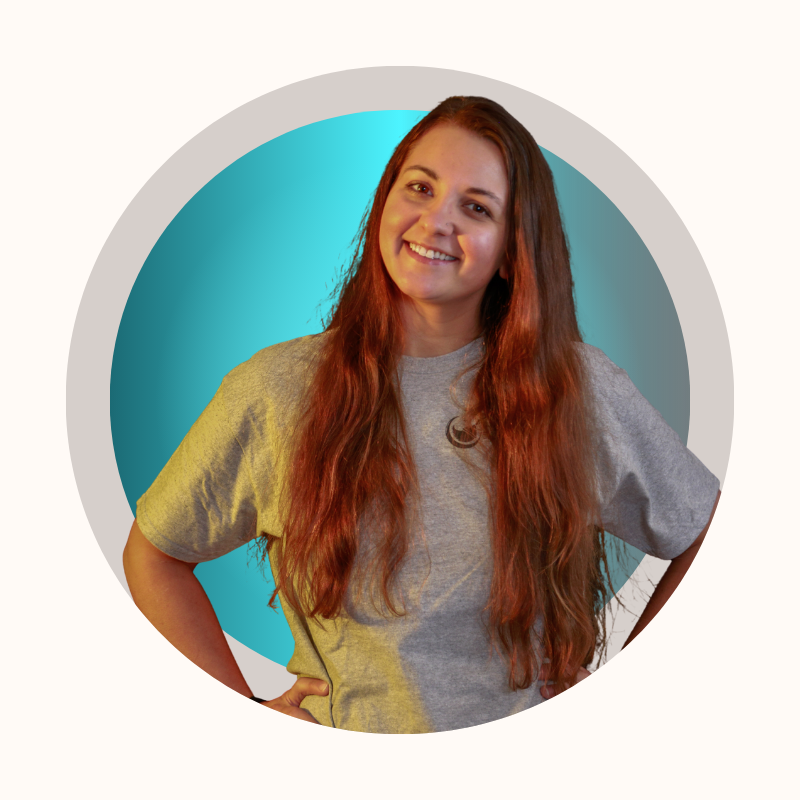 Woman with long red hair, smiling, wearing a gray t-shirt, hands on hips, set against a teal and white background.