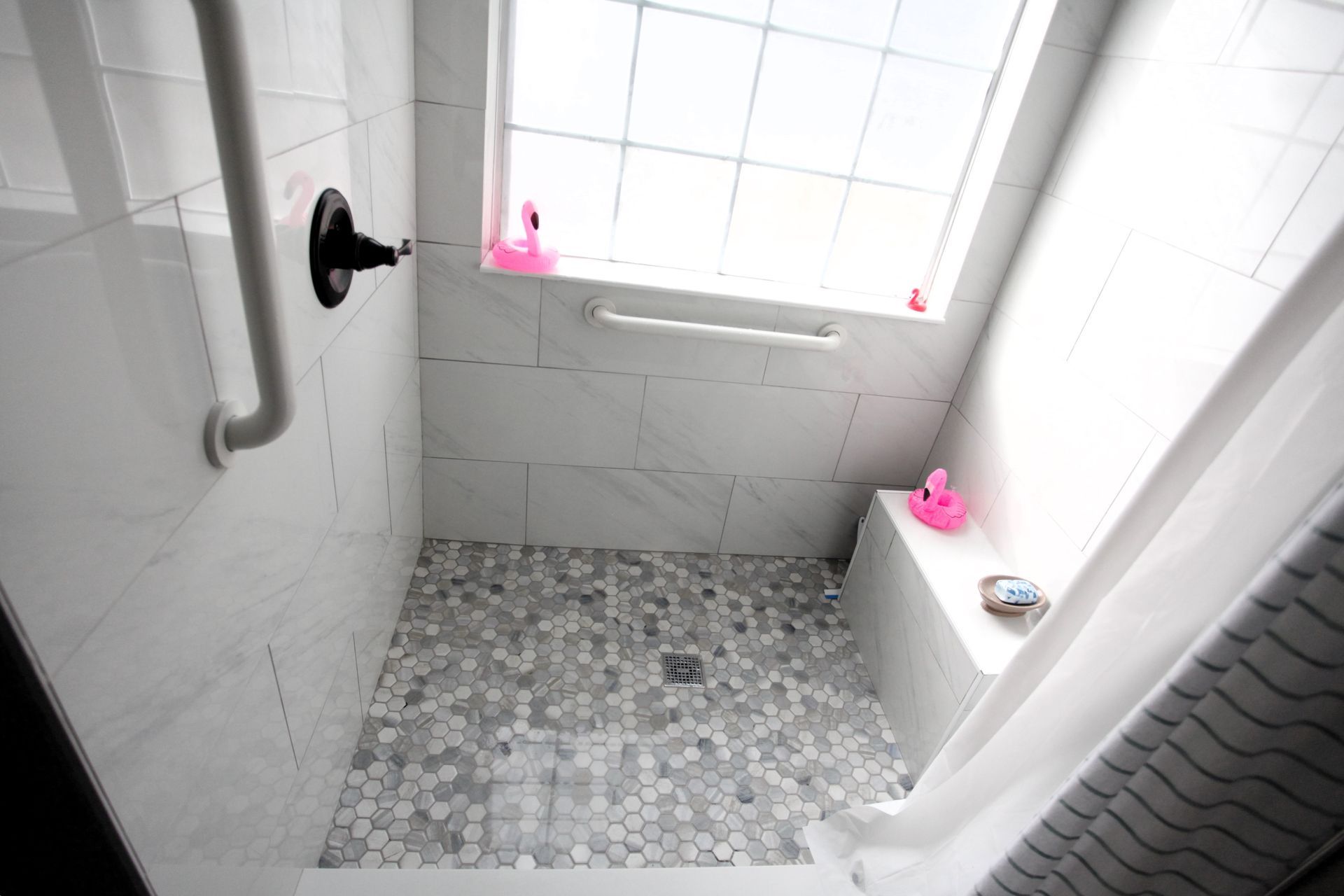 Shower stall with white tile walls and pebbled floor, a window, and a shower curtain.