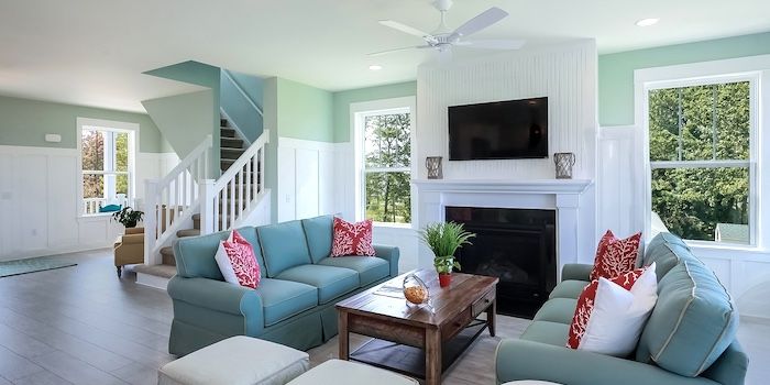 Living room with teal sofas, a fireplace, and a staircase. The walls are white and light green.