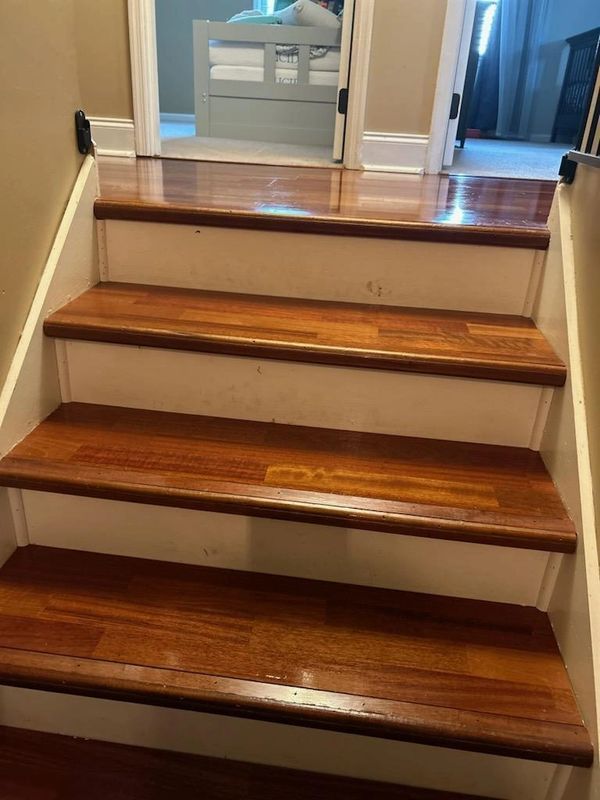 Wooden stairs with white risers lead to a hallway with a bed visible.