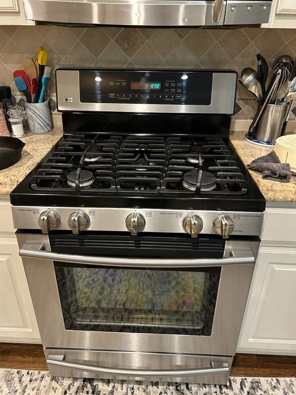 Stainless steel gas range in a kitchen. Black cooktop with 5 burners, oven below, and digital display.