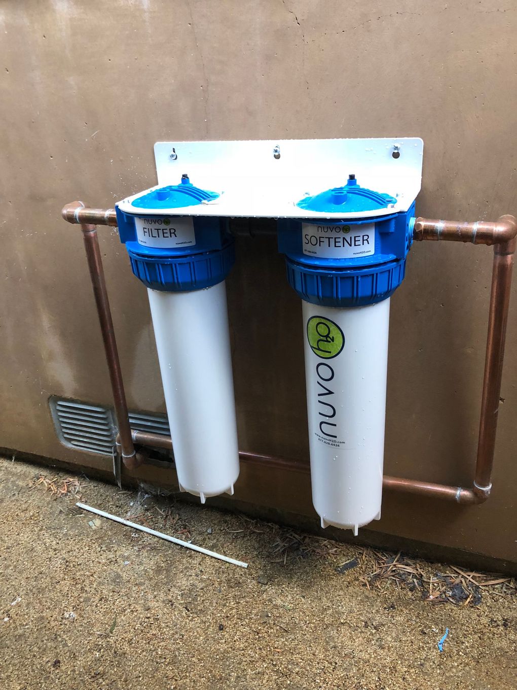 A water filter is hanging on a wall next to a copper pipe.