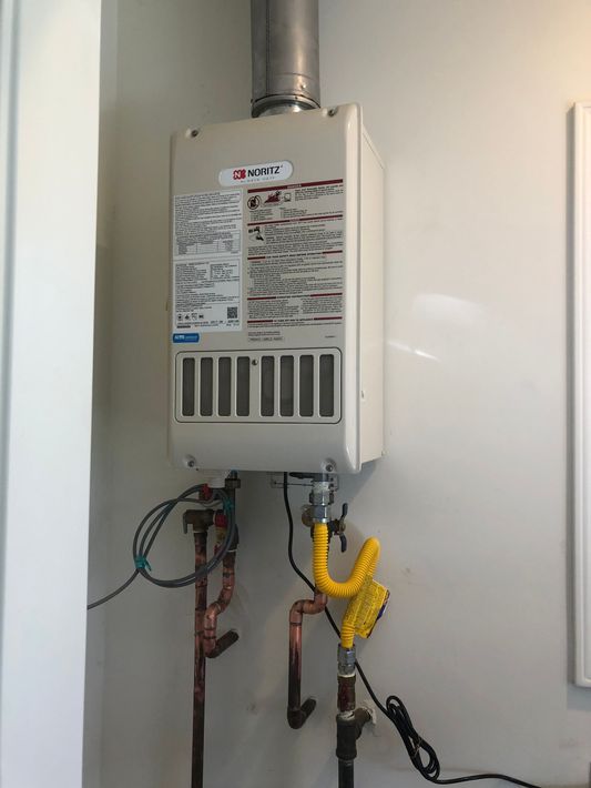 A water heater is hanging on a wall next to a gas pipe.