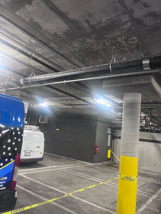 A blue van is parked in a parking garage next to a yellow pole.
