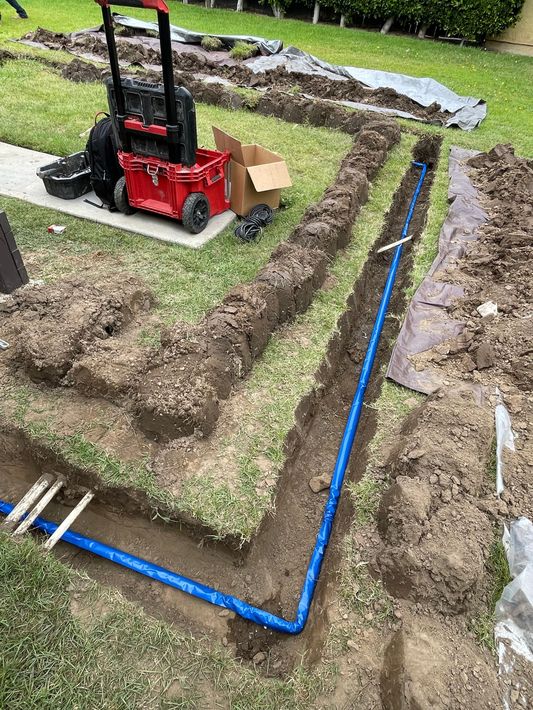 A blue pipe is being installed in the dirt in a yard.