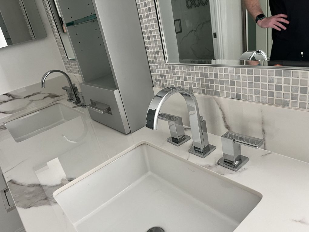 A man is taking a selfie in a bathroom with a sink and mirror.