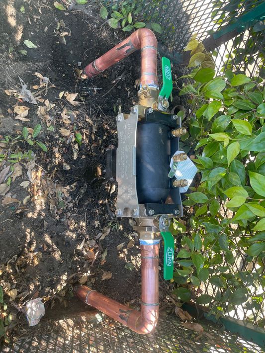 A copper pipe with a green valve is sitting in the dirt.