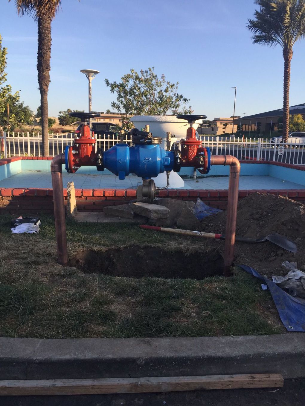 A blue water meter is sitting in the grass near a pool