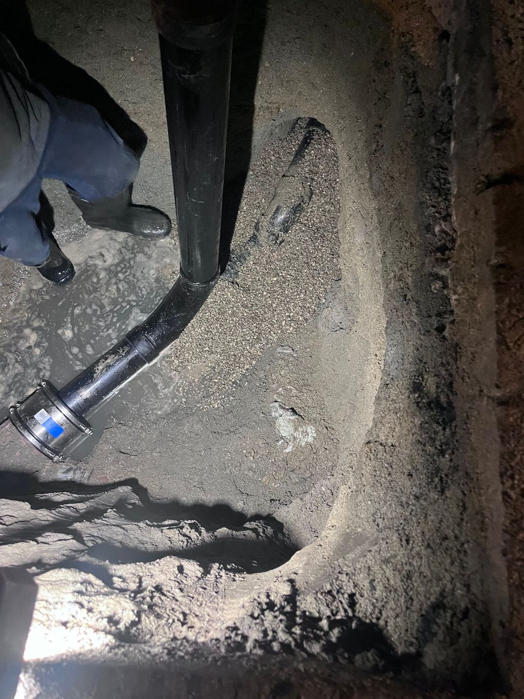 A person is standing next to a pipe in a hole in the ground.