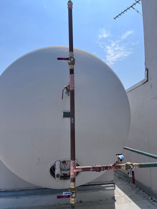 A large white tank with pipes attached to it is sitting next to a building.