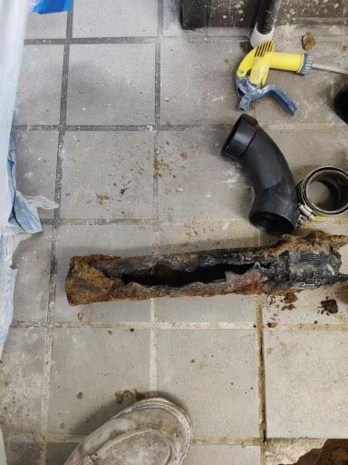 A rusty pipe is sitting on a tiled floor next to a hose.