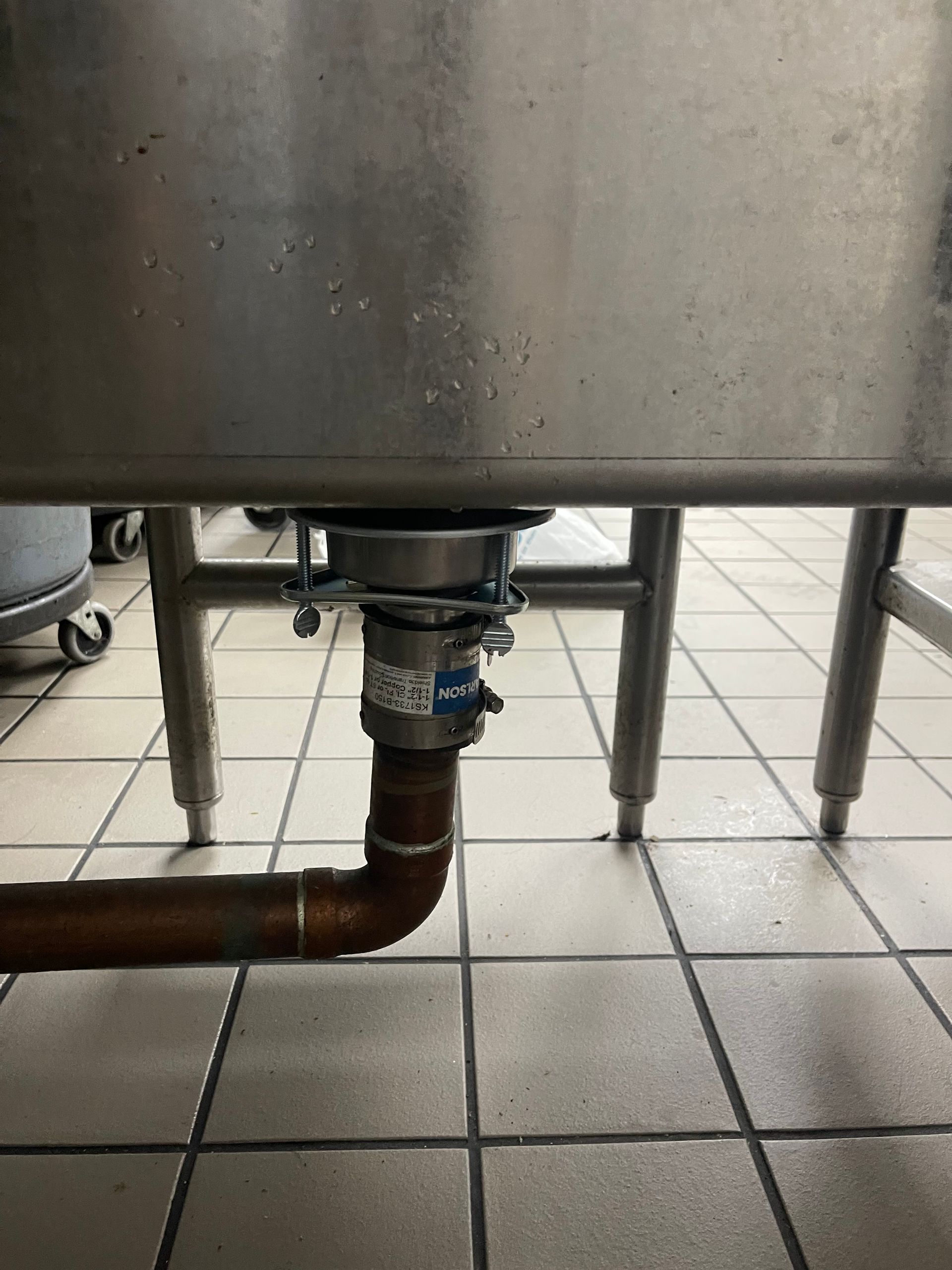 A stainless steel sink with a copper pipe underneath it.
