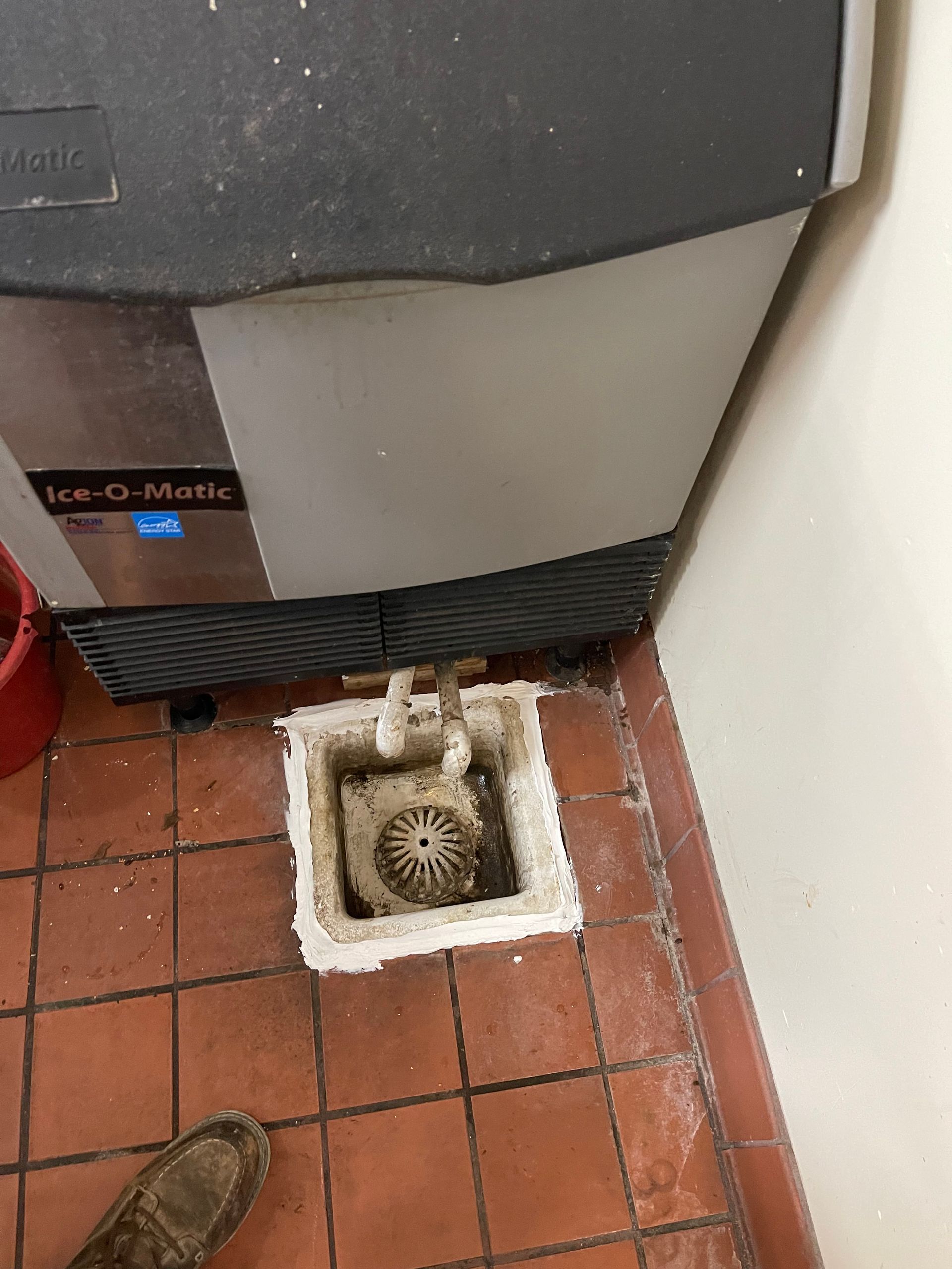 A dirty ice machine is sitting on a tiled floor.