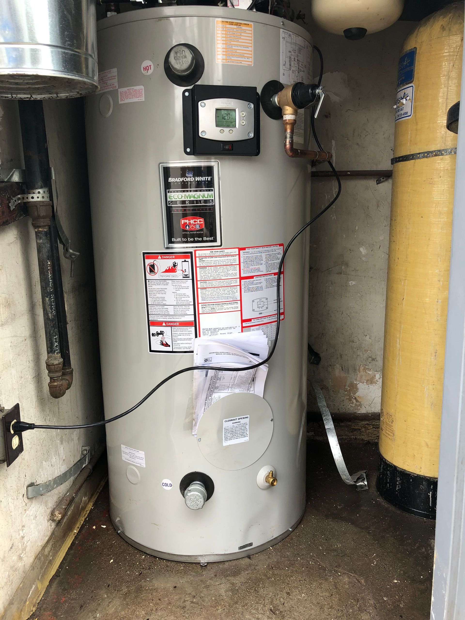 A water heater is sitting in a room next to a yellow tank.