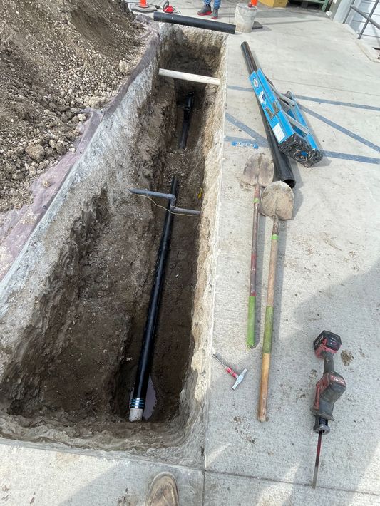A hole in the ground with a pipe in it and tools on the ground.