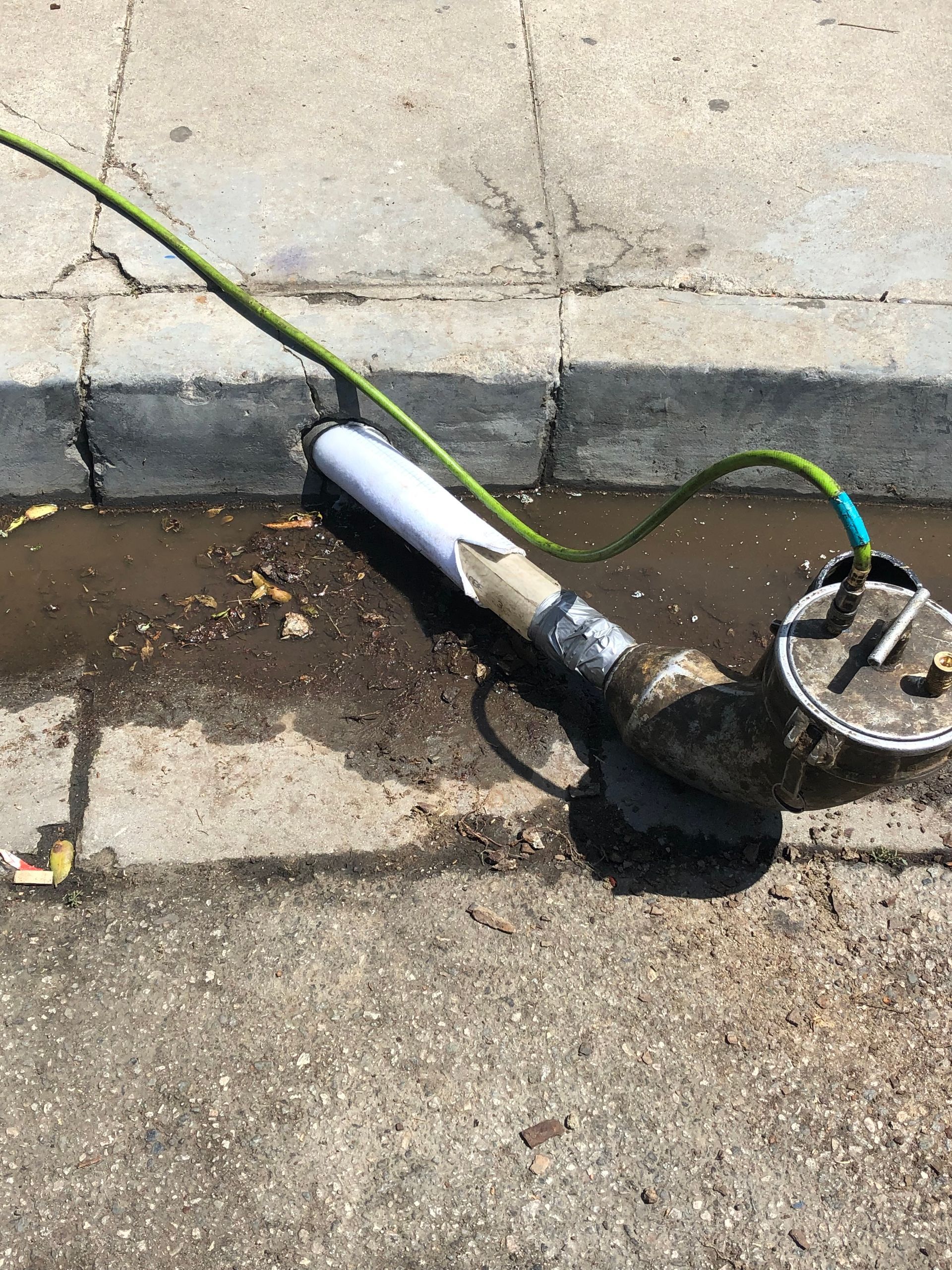 A pipe with a green hose attached to it is laying on the ground.