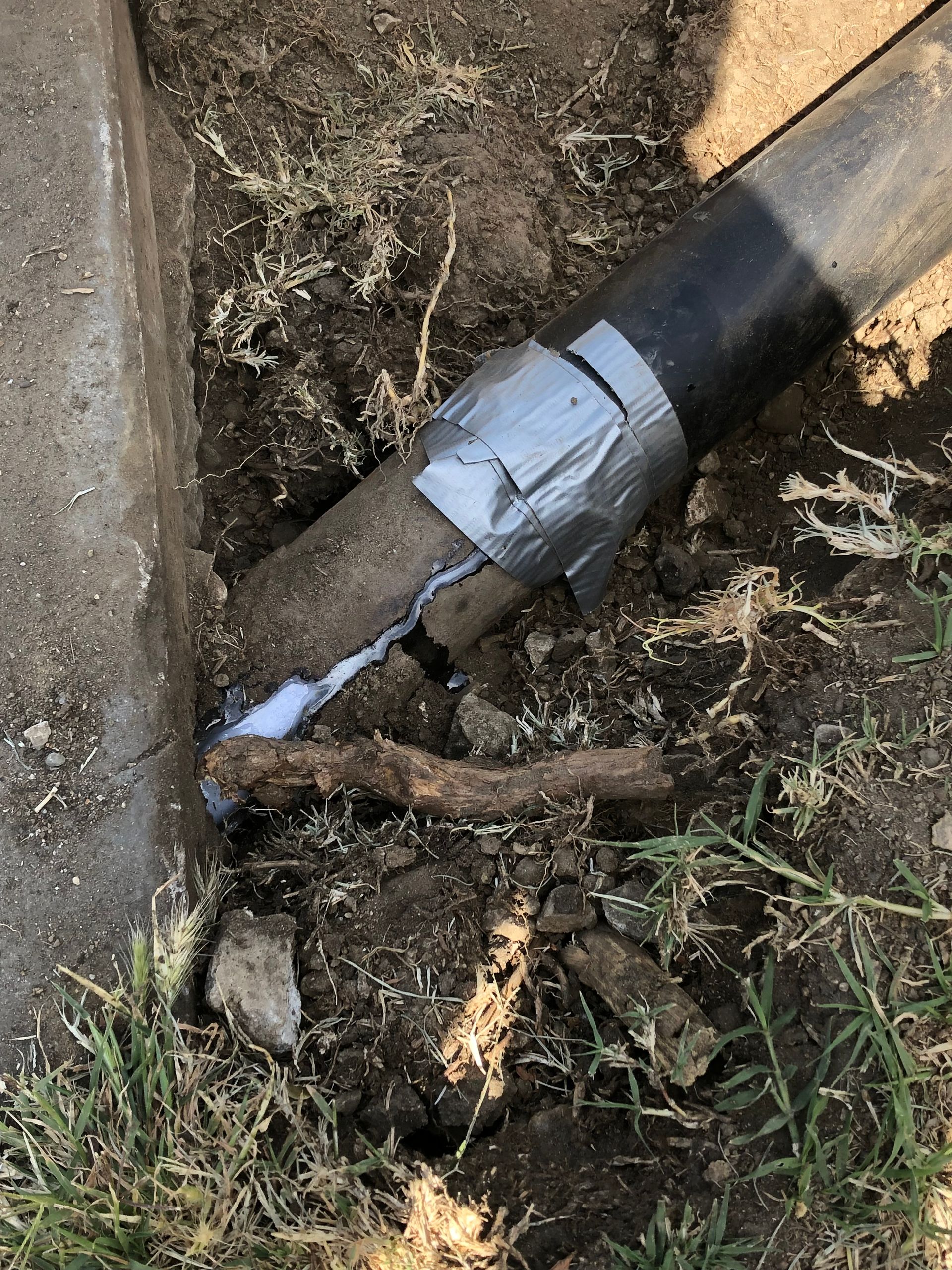 A pipe with duct tape on it is laying in the dirt.