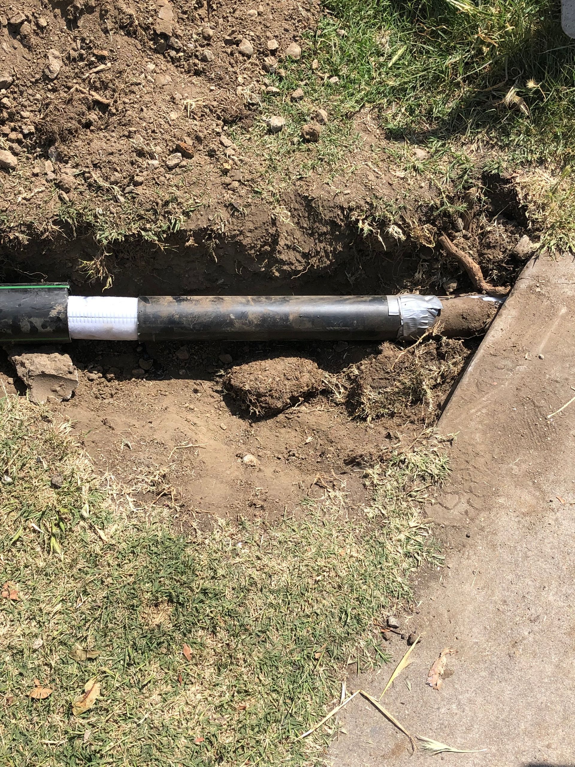 A black pipe is sitting in the dirt next to a sidewalk.
