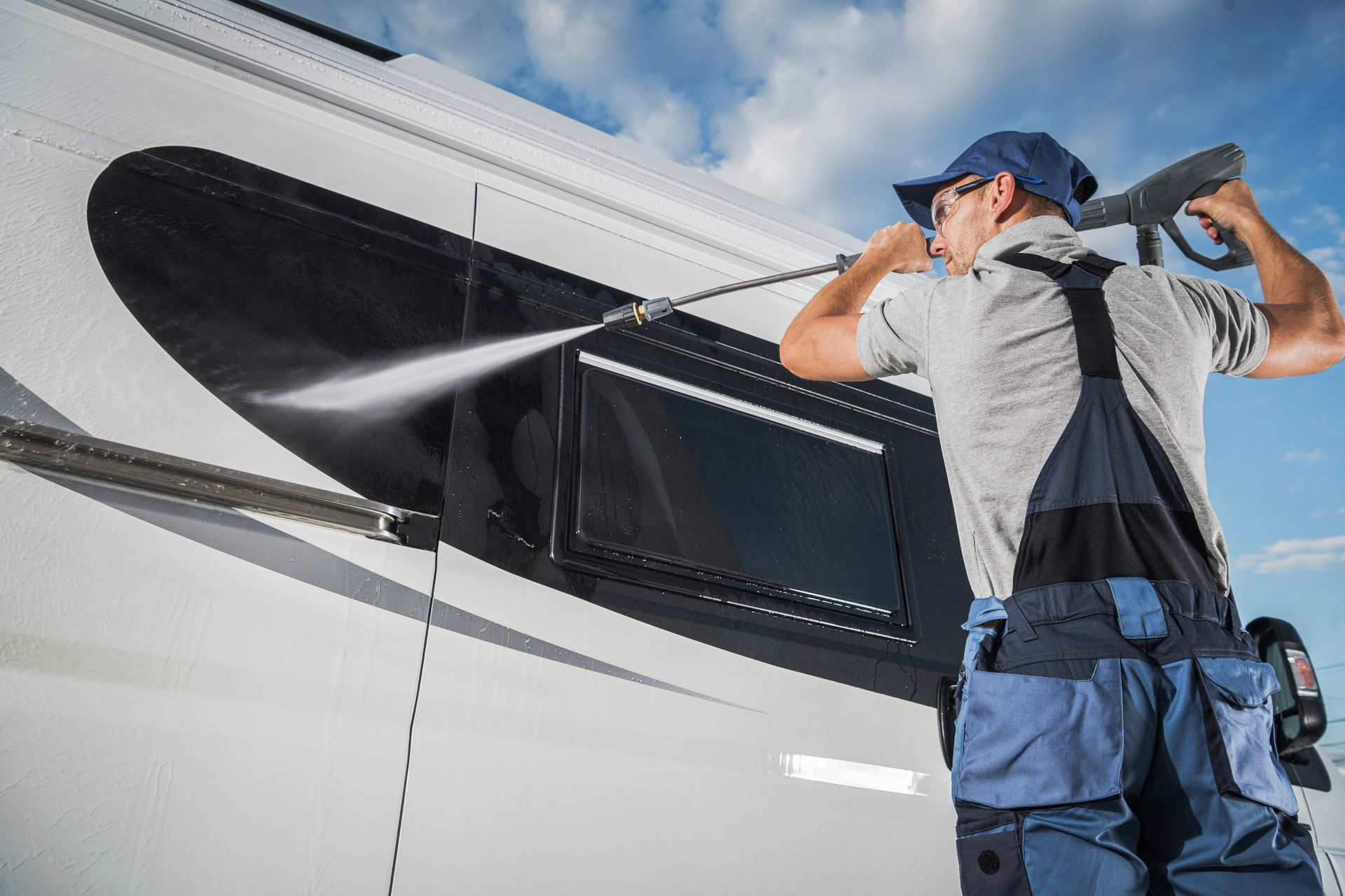 A man is cleaning a camper van with a high pressure washer.