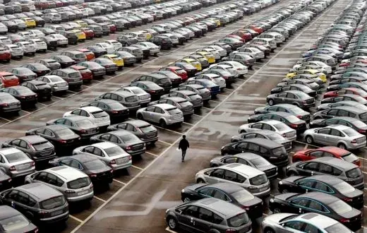 A man is walking through a parking lot filled with lots of cars.