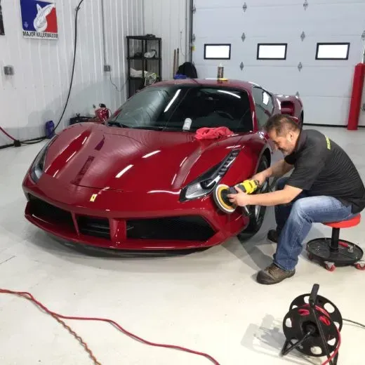 A man is polishing a red sports car in a garage