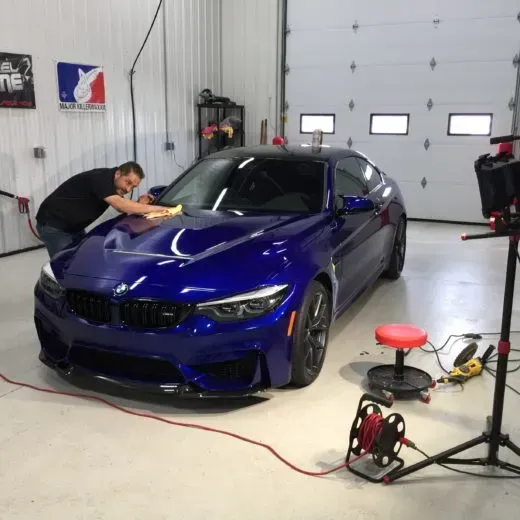 A man is polishing a blue car in a garage