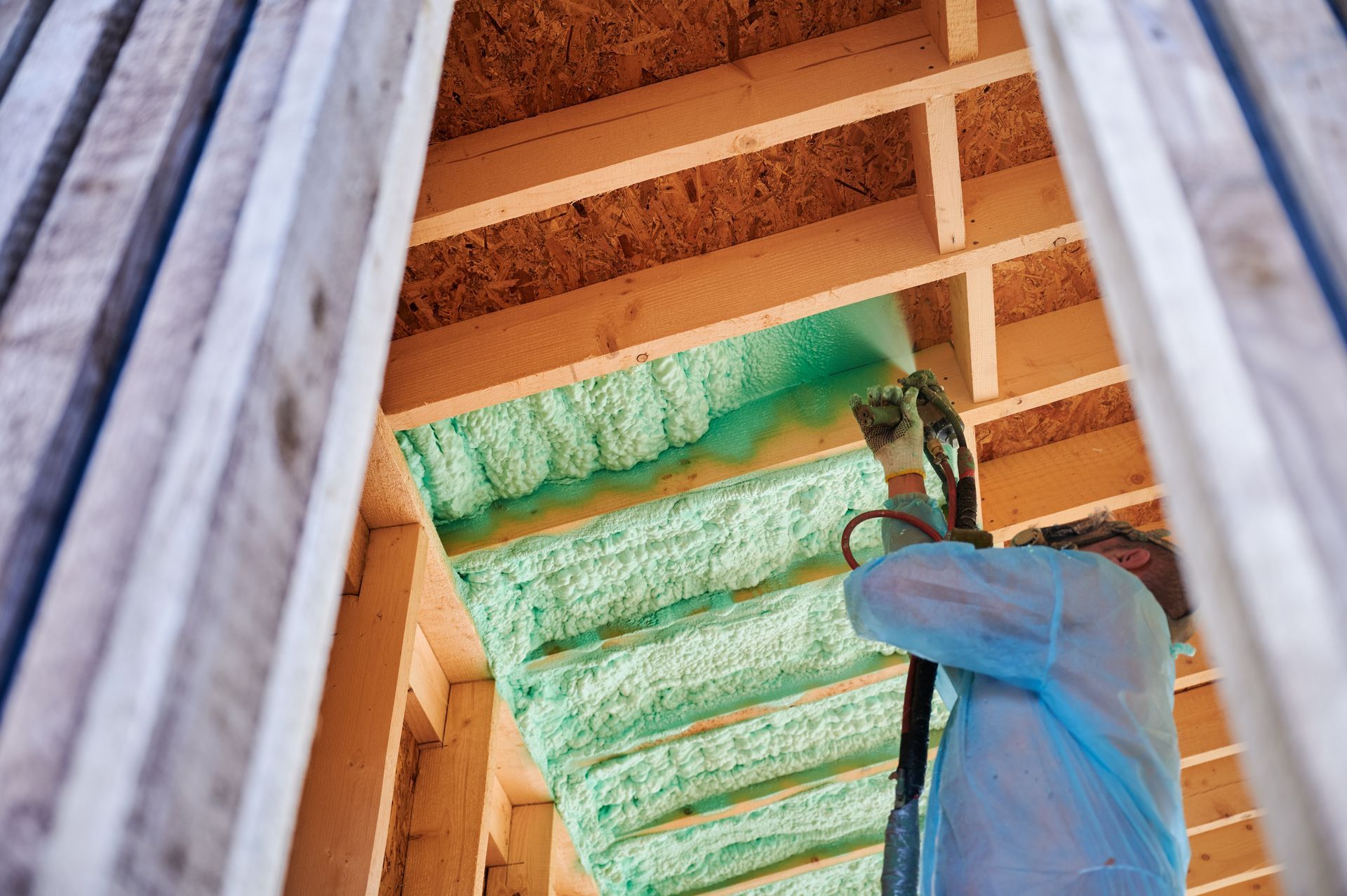 A person is spraying green insulation on a wooden ceiling.