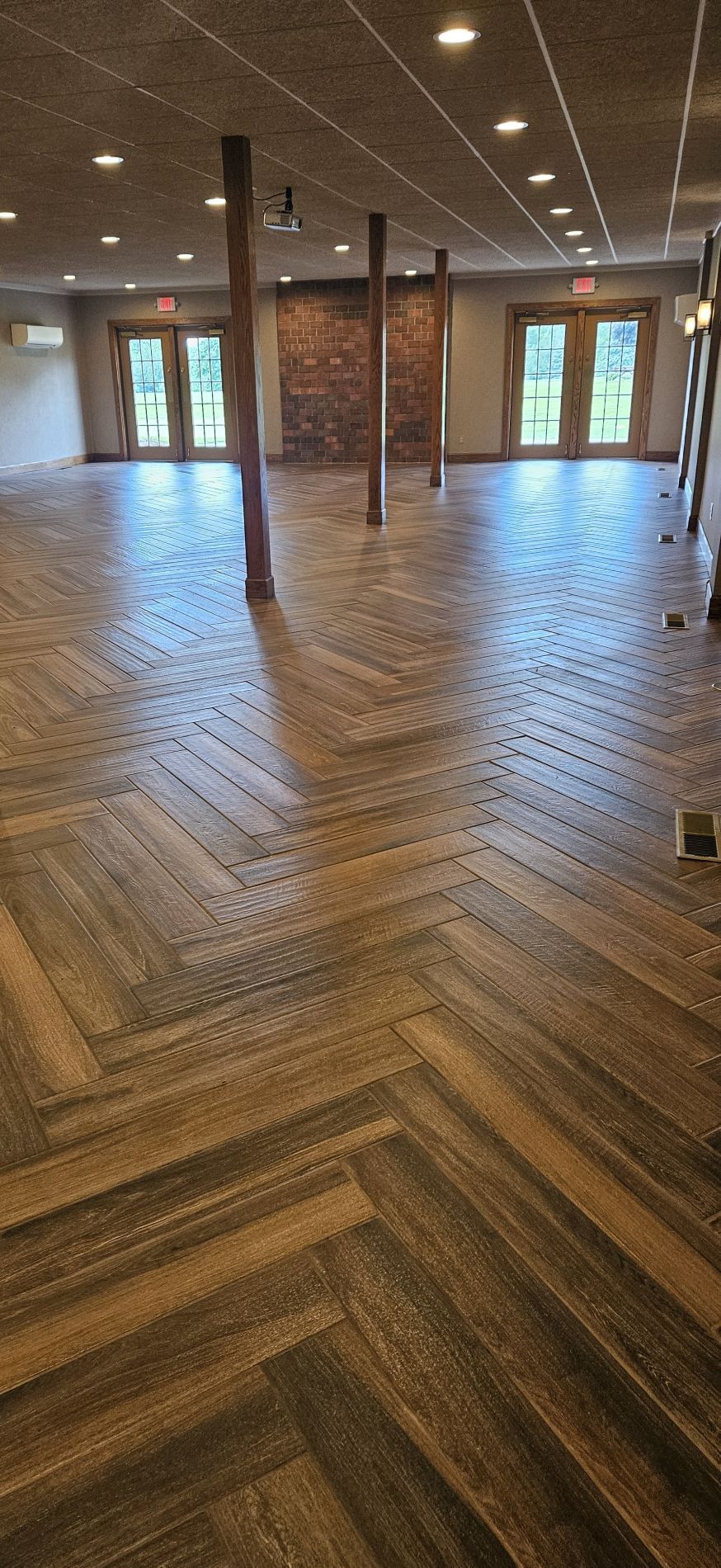Herringbone wood floor in a large room with columns and exposed brick wall.