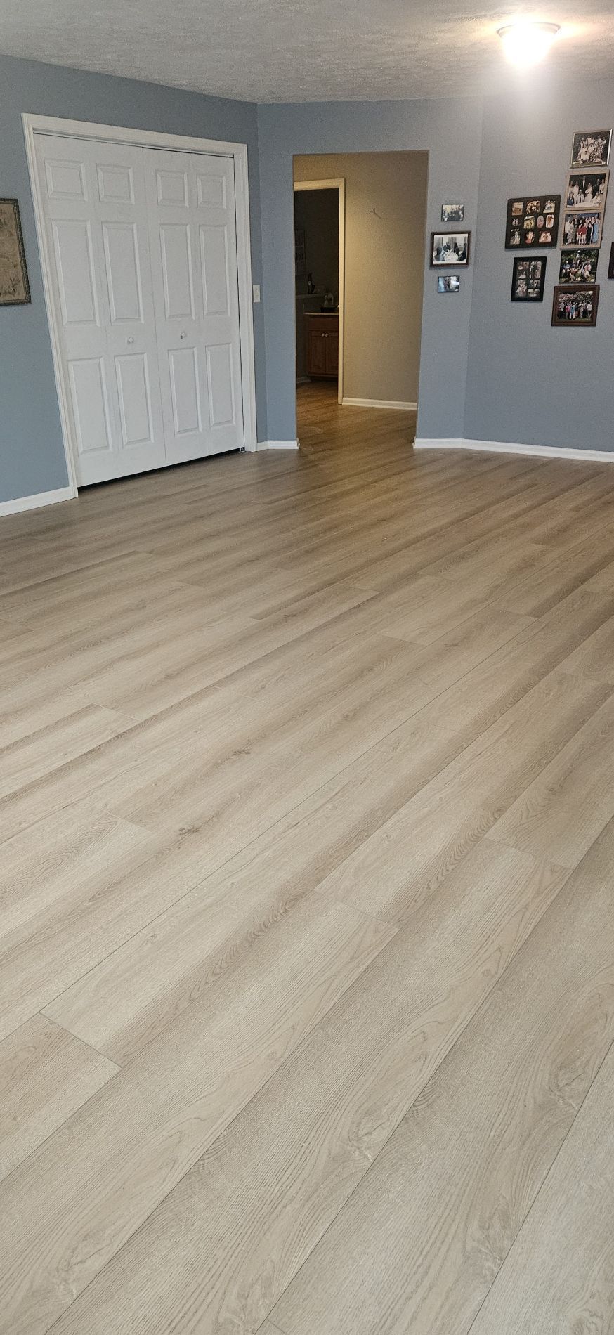 Room with light wood-look flooring and blue walls. White closet doors and a doorway to another room are visible.