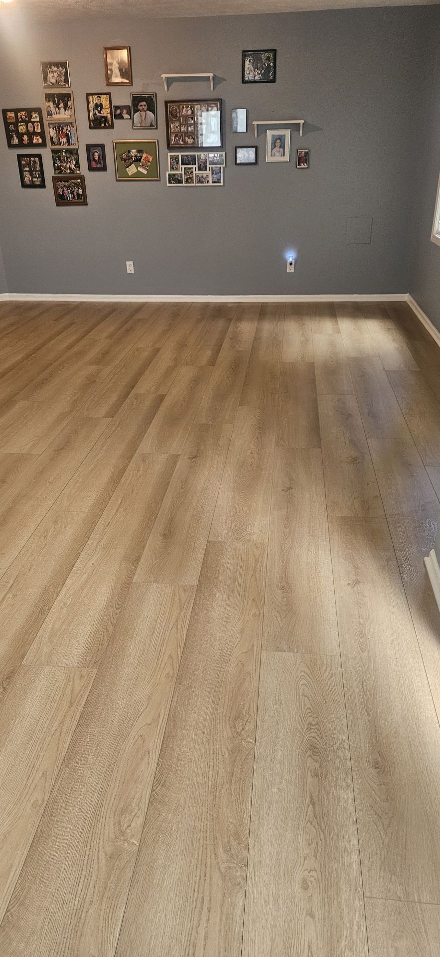 A room with light brown wooden floors and a gray wall with framed pictures.