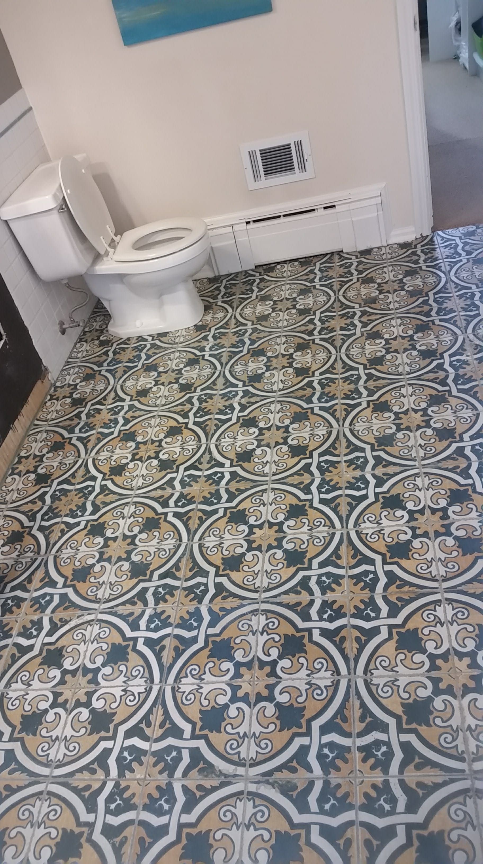 Bathroom with patterned blue, tan, and white floor tiles. White toilet, walls, and vent.