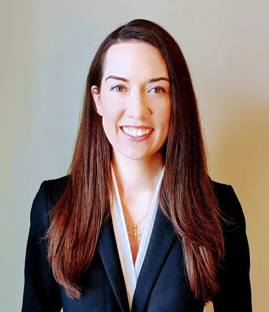 Woman in a black blazer smiling against a plain beige background.