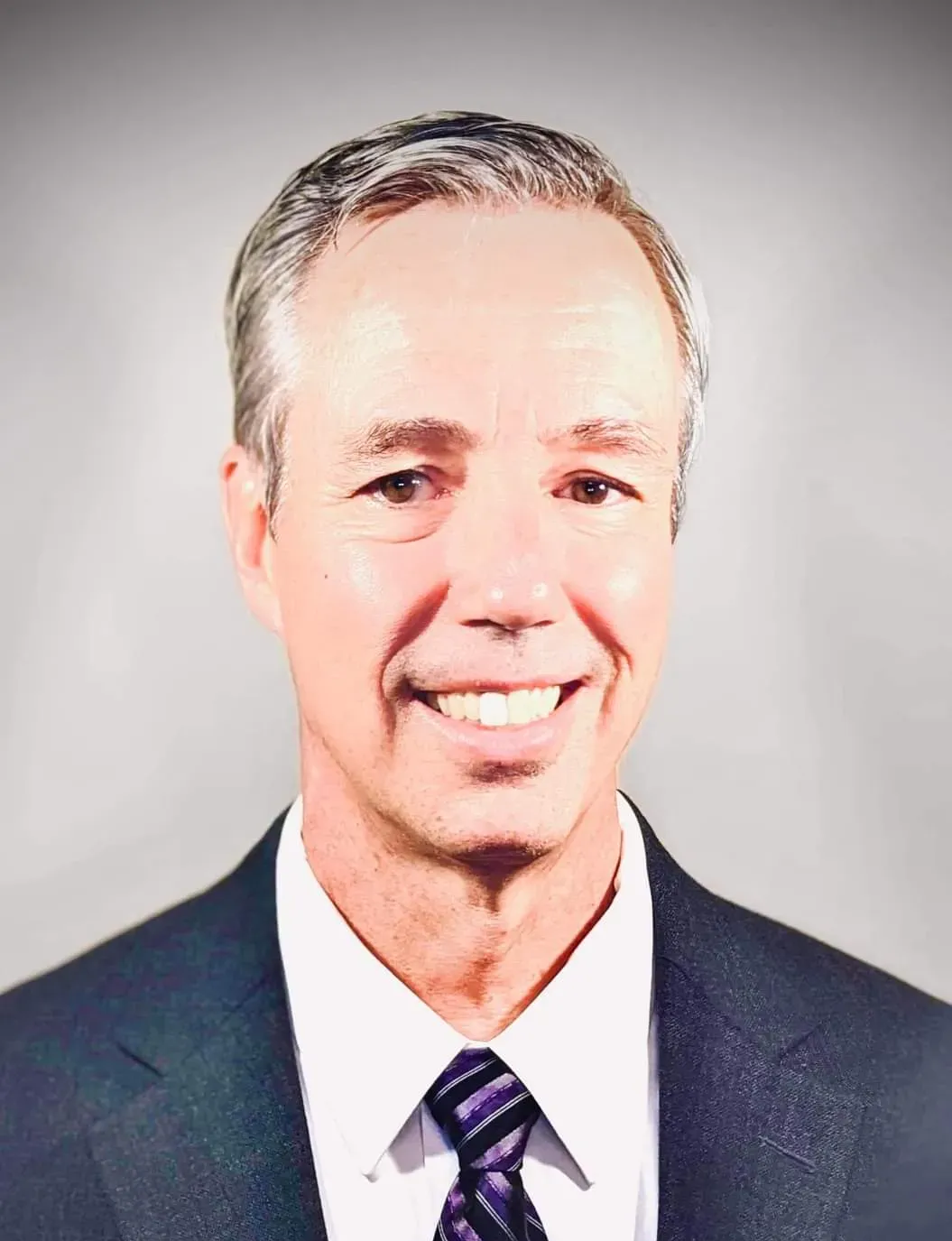 Smiling man in a dark suit and tie against a light gray background