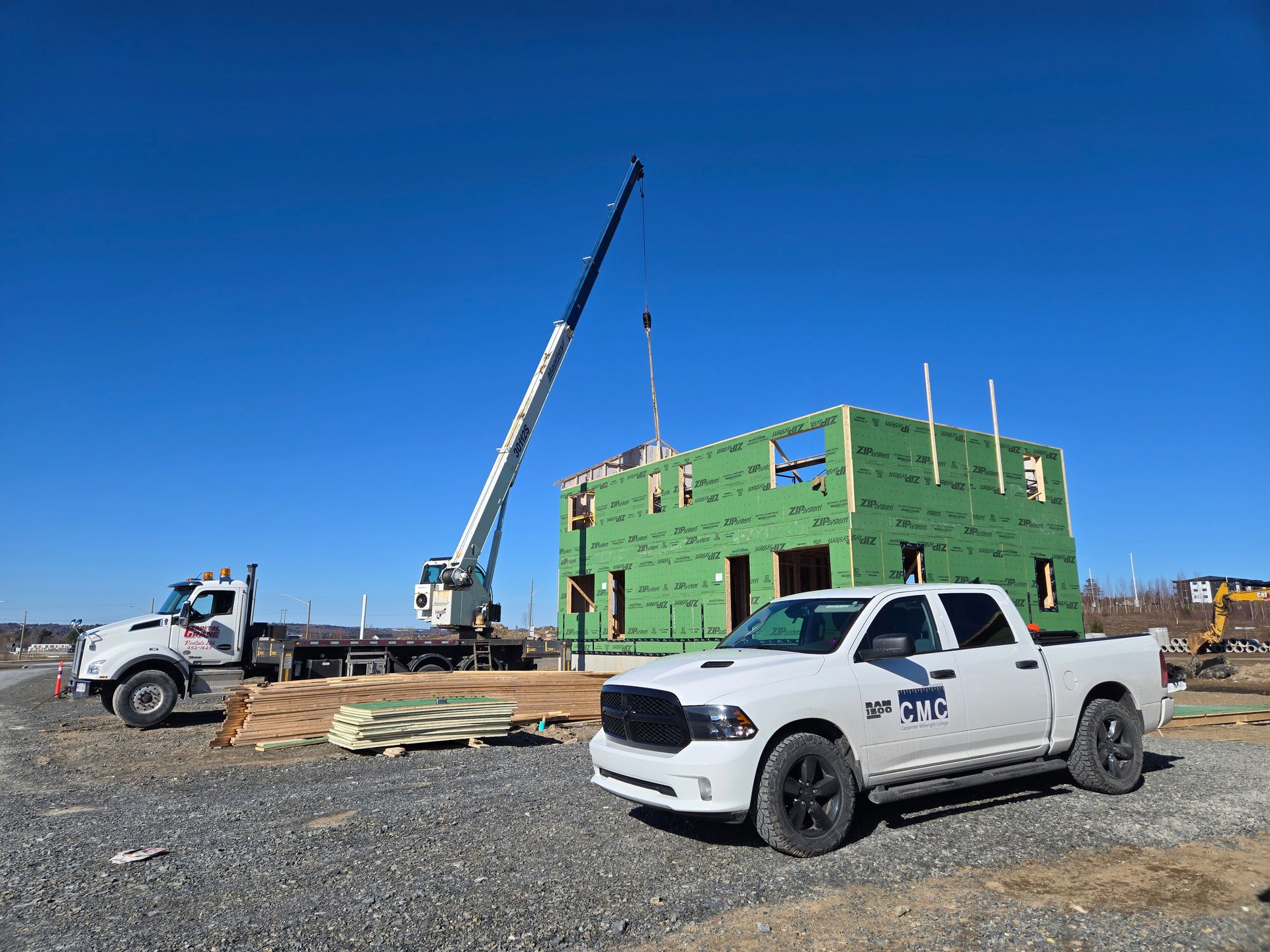 Habitat New Brunswick, Construction site with green house framing, crane, and two pickup trucks on gravel