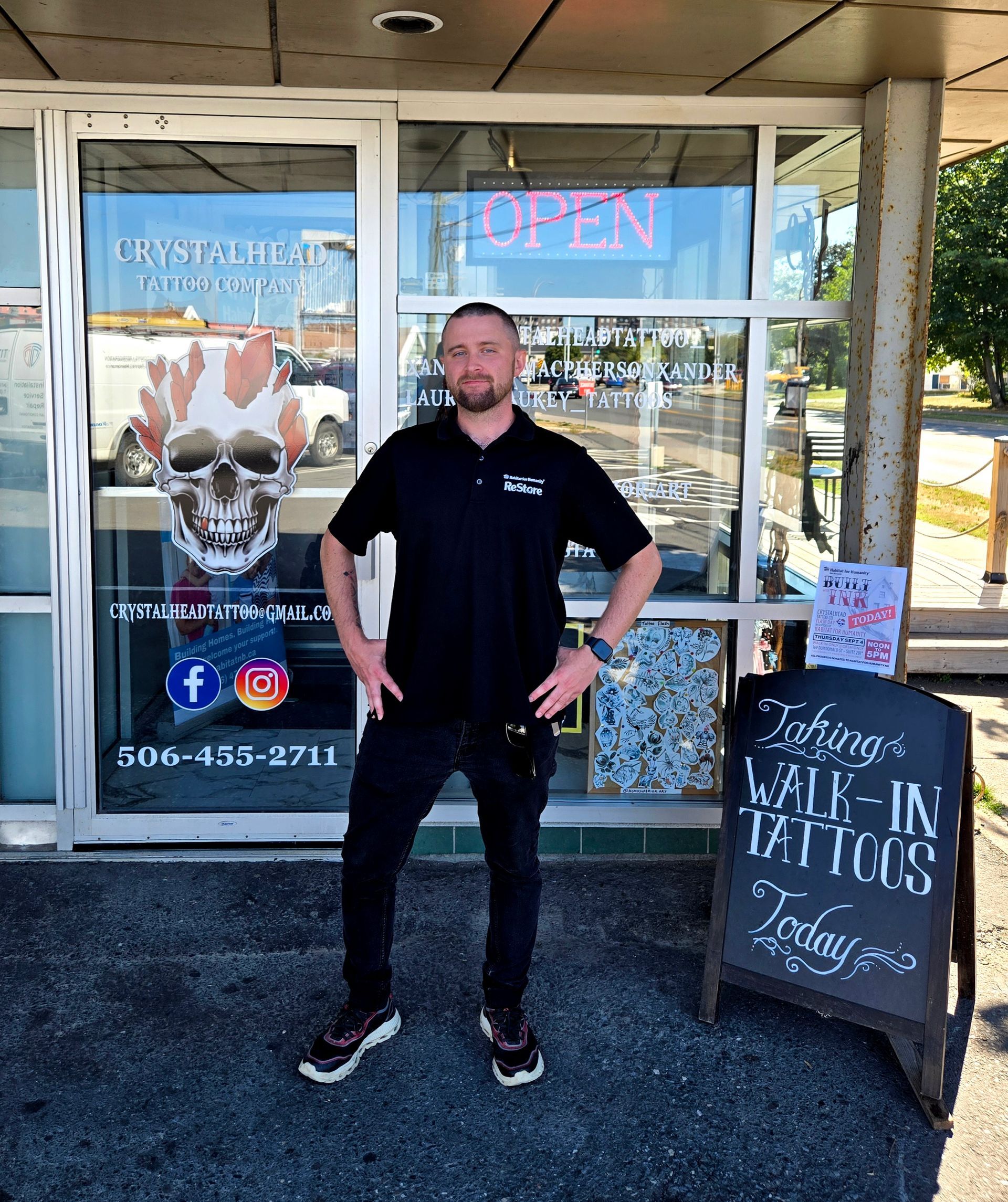 Habitat New Brunswick volunteer standing outside a storefront with an OPEN sign, hands on hips smiling