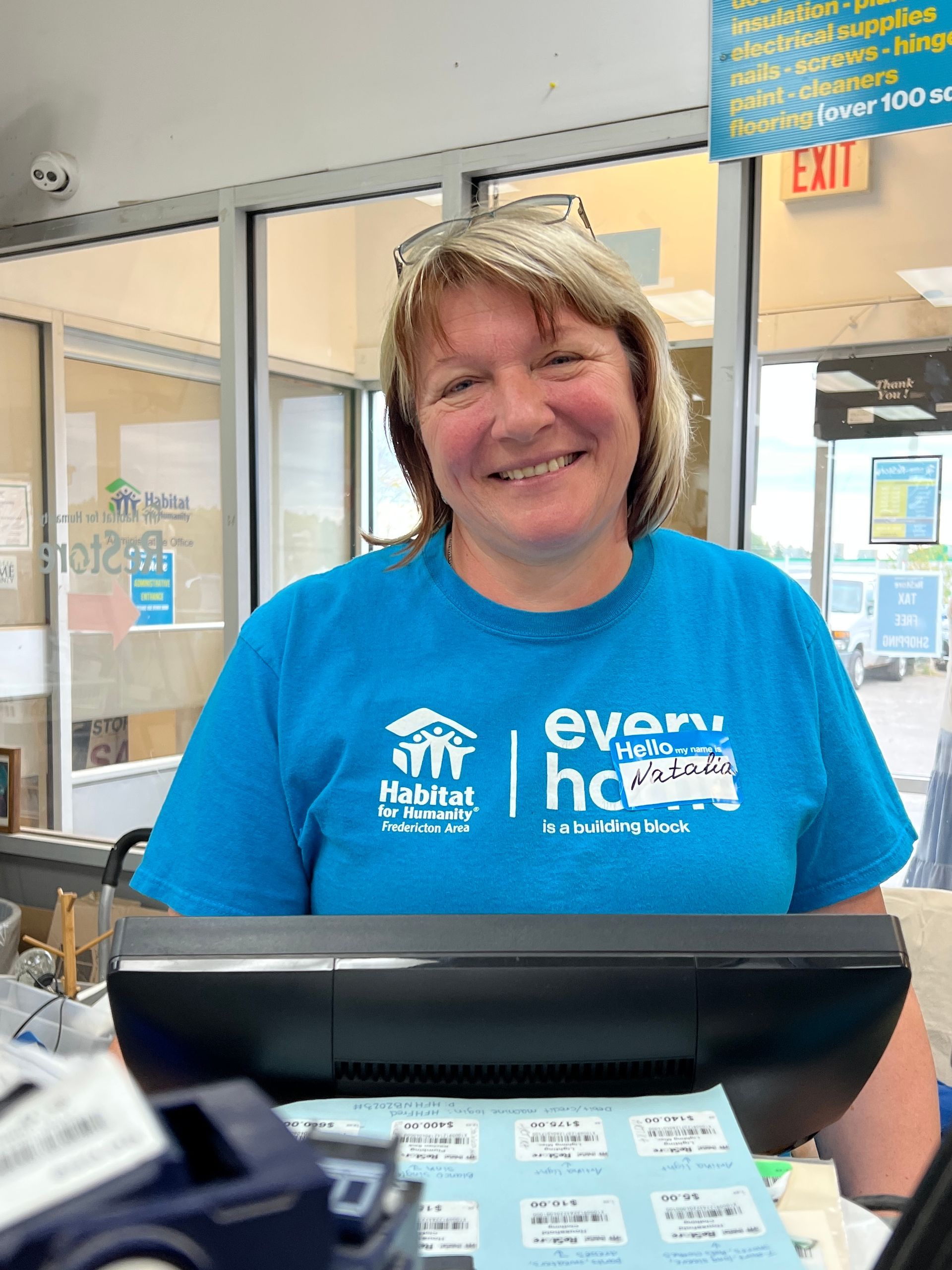 Habitat New Brunswick volunteer Smiling in a blue T-shirt standing behind a store counter.