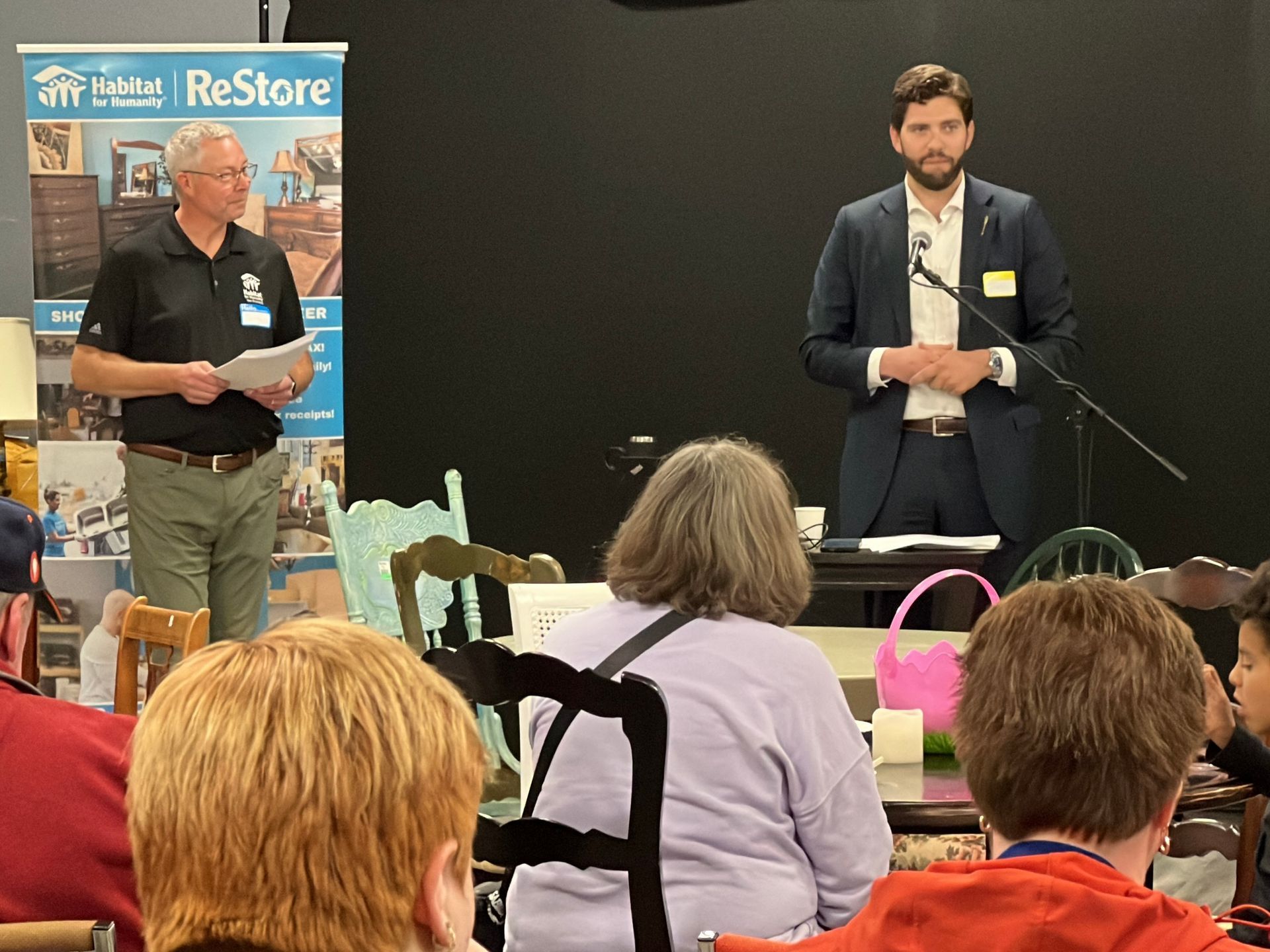 Two men speak at a Habitat New Brunswick panel event, with audience members seated in the foreground.