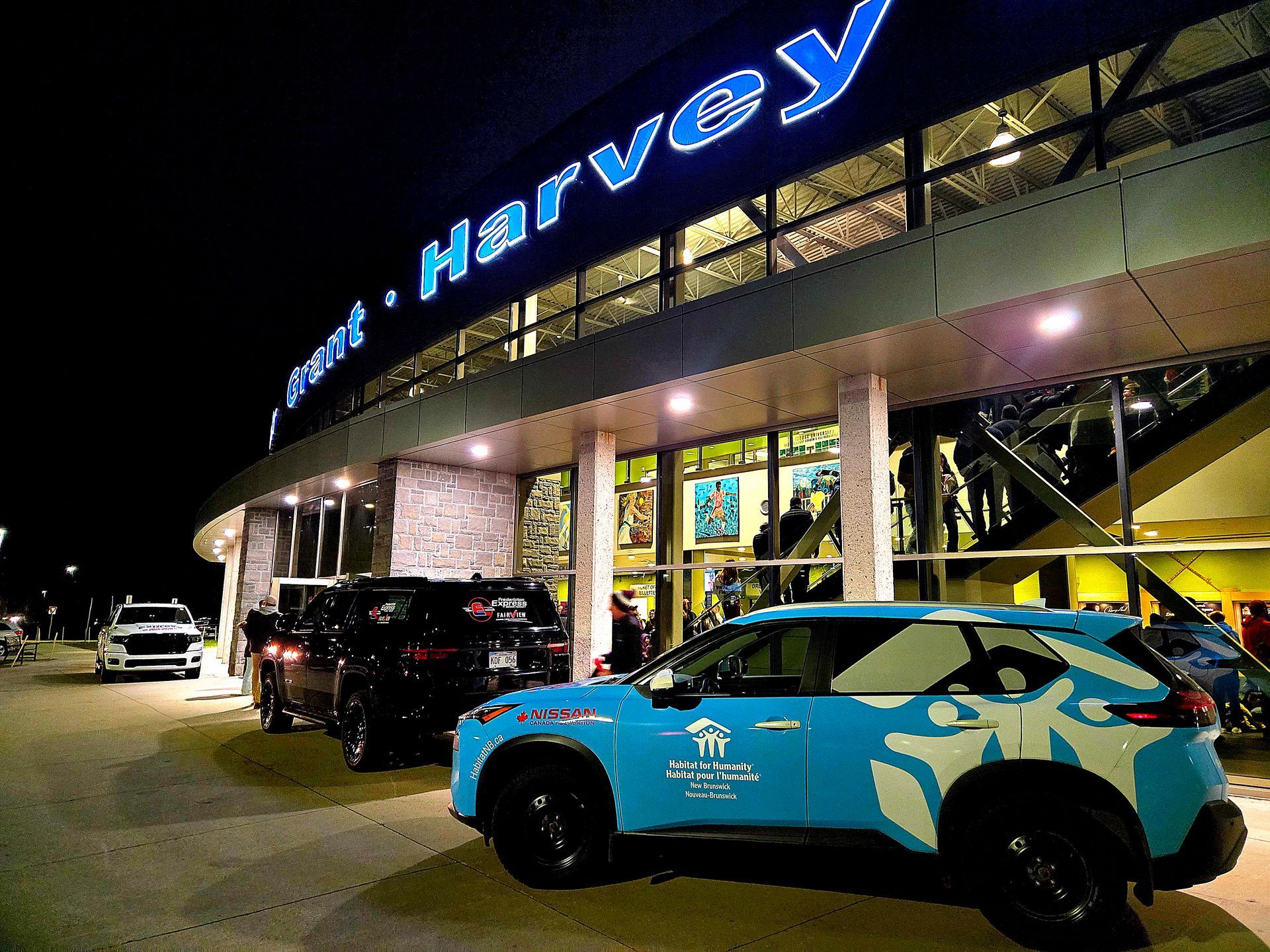 Nighttime outside a Harvey store with parked cars, including a blue-and-black Habitat New Brunswick car in front.