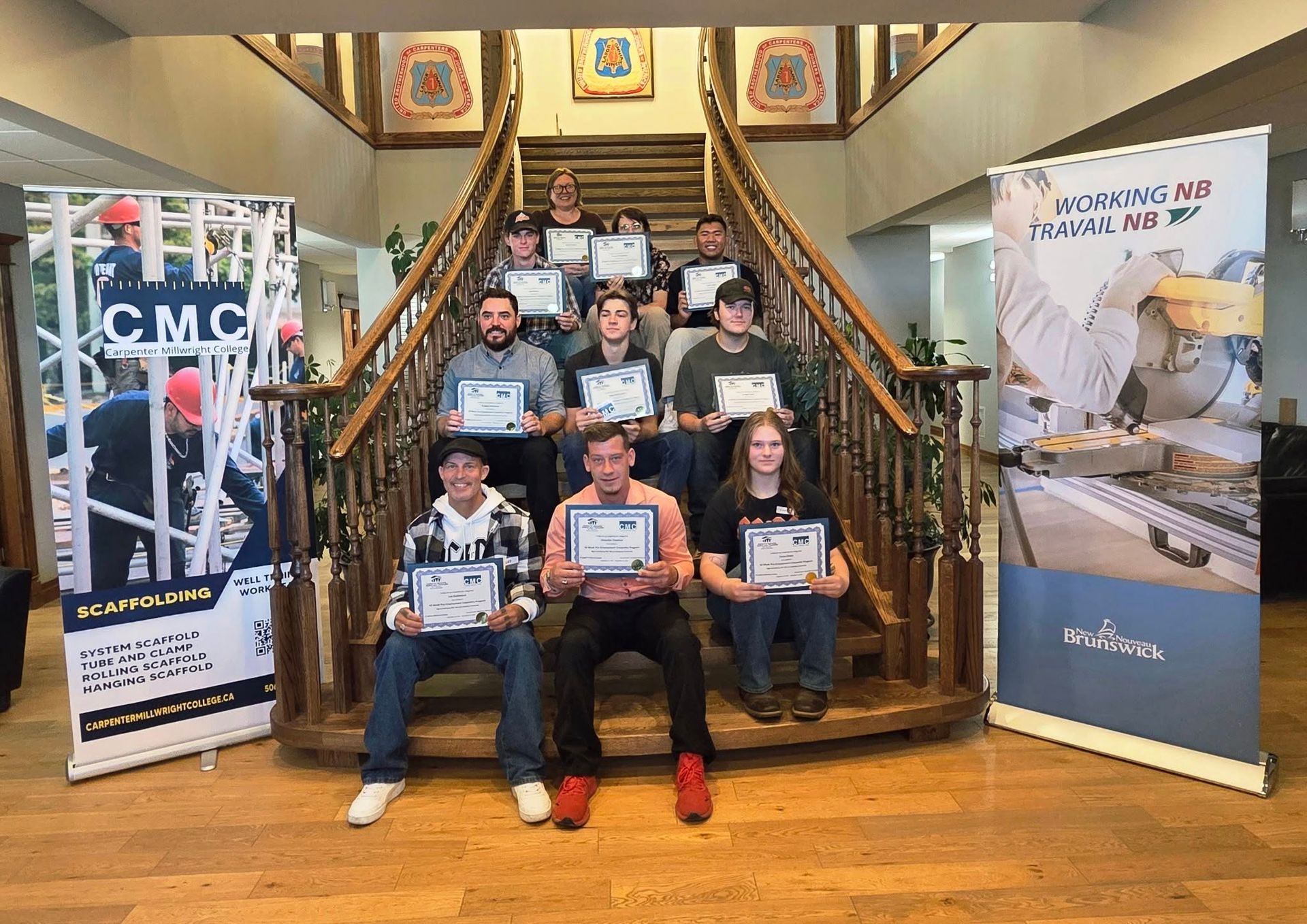 Students pose on a staircase holding awards at a CAC event banner display.