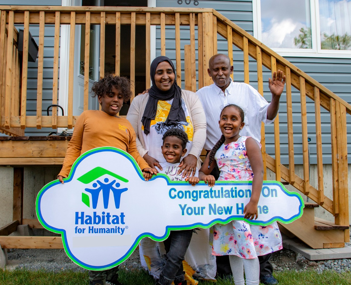 Habitat for Humanity New Brunswick family of 5 smiling standing together outside of their new home.