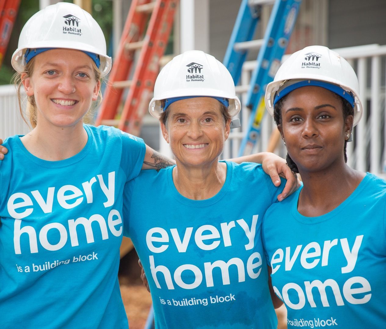 Habitat New Brunswick, Three volunteers in white hard hats wearing blue “every home” T-shirts at a construction site