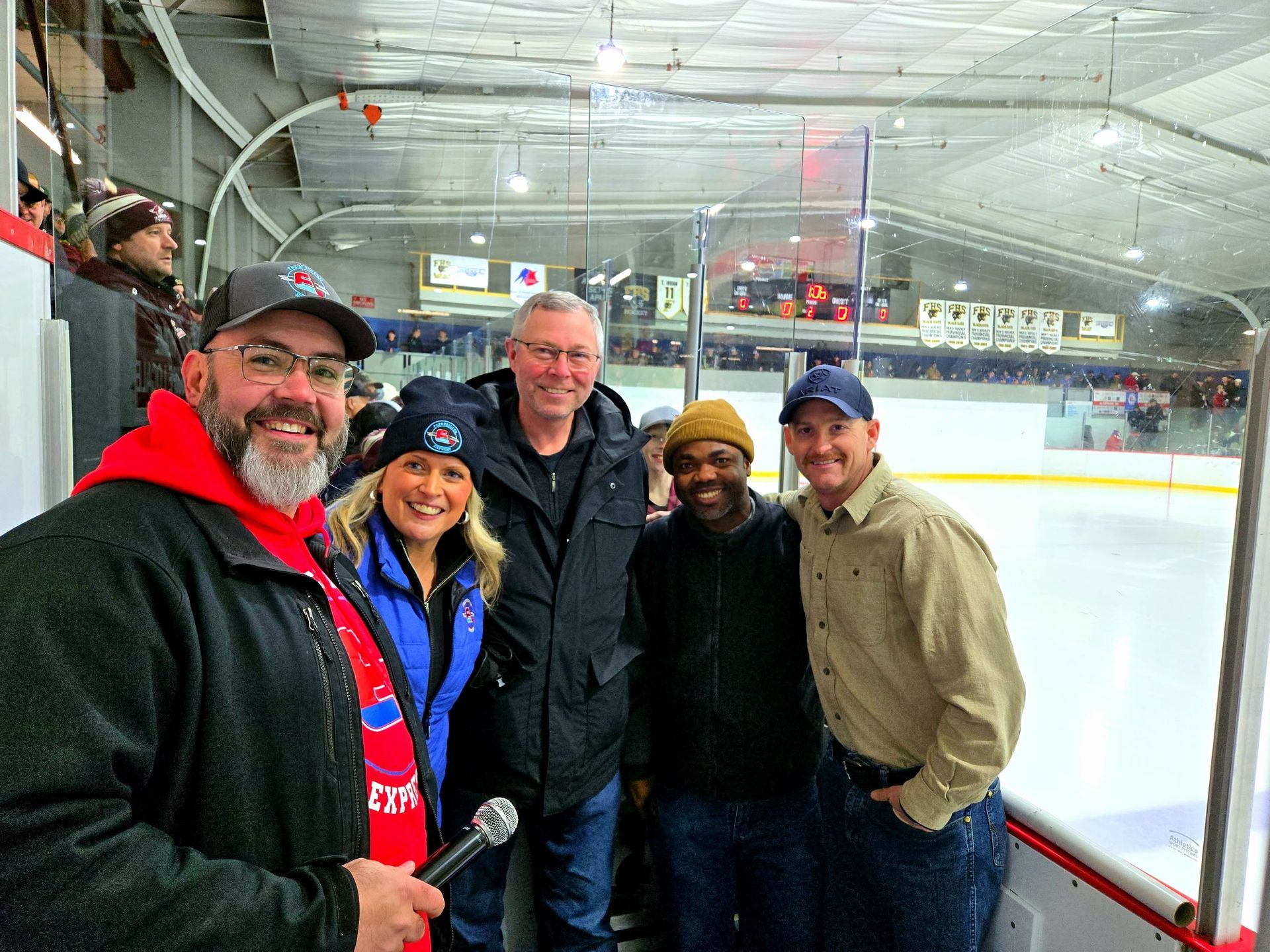 Habitat New Brunswick, Five people smiling on an indoor ice rink, posing in winter jackets and hats.