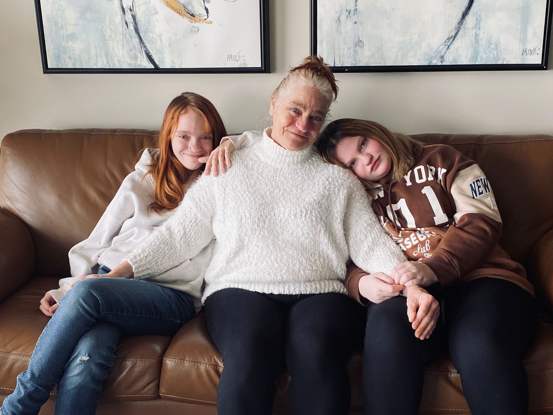 Habitat New Brunswick partner family of 3 sit close together on a brown leather couch, smiling in a cozy living room.
