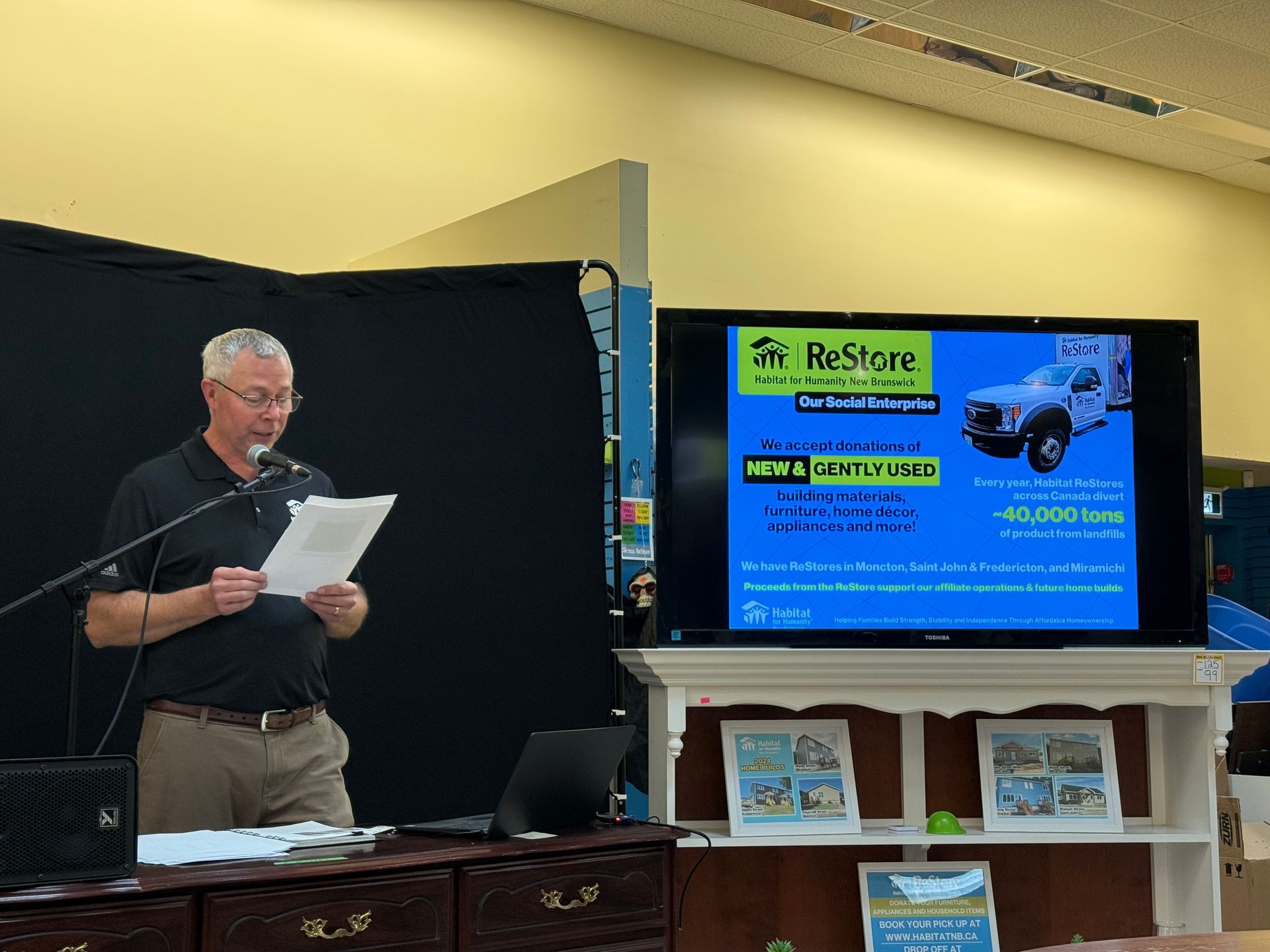 Perry presenting beside a large display screen with a service truck slide at an indoor event
