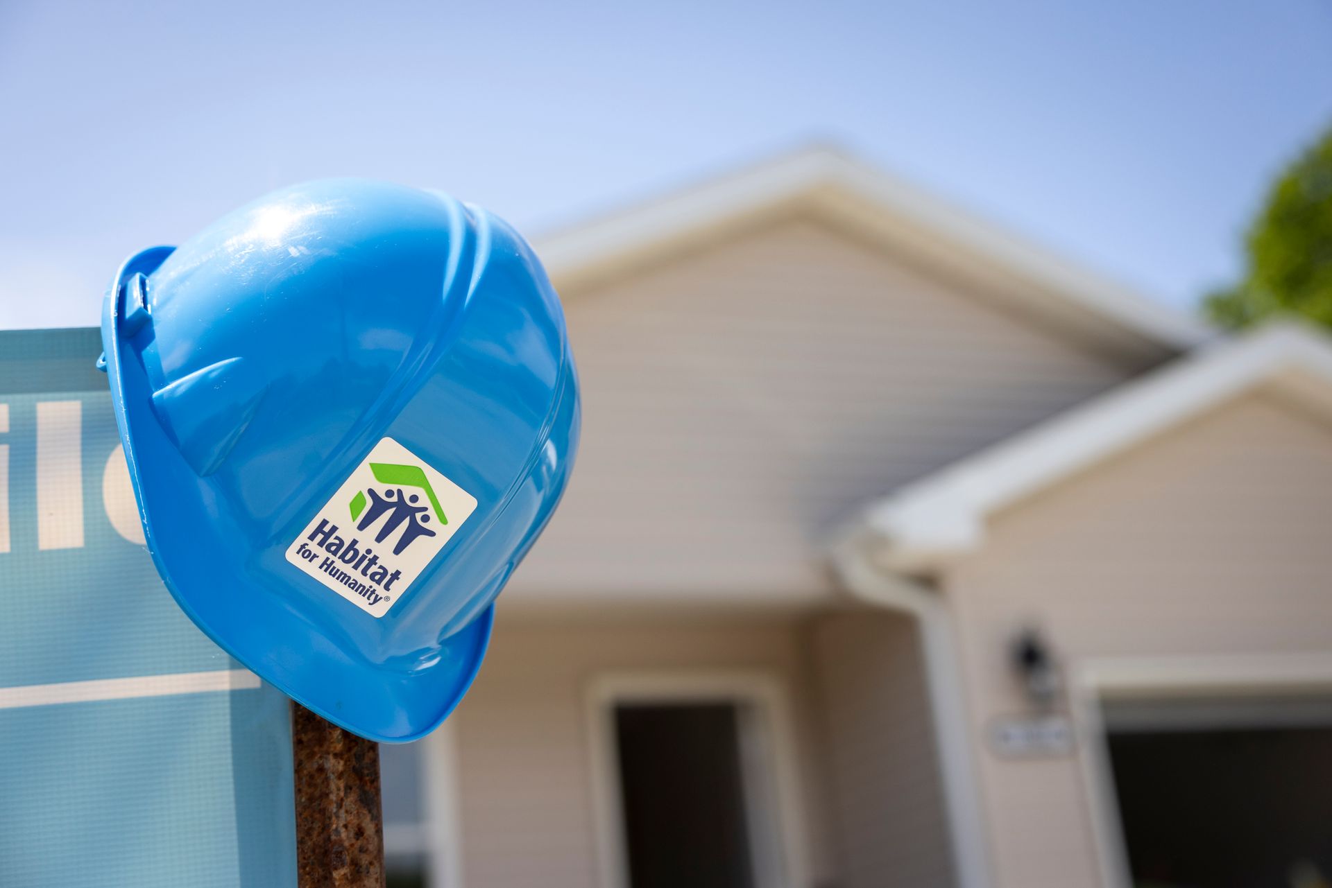 Habitat New Brunswick Blue hard hat on a post in front of a house, with a blurred sign in the background