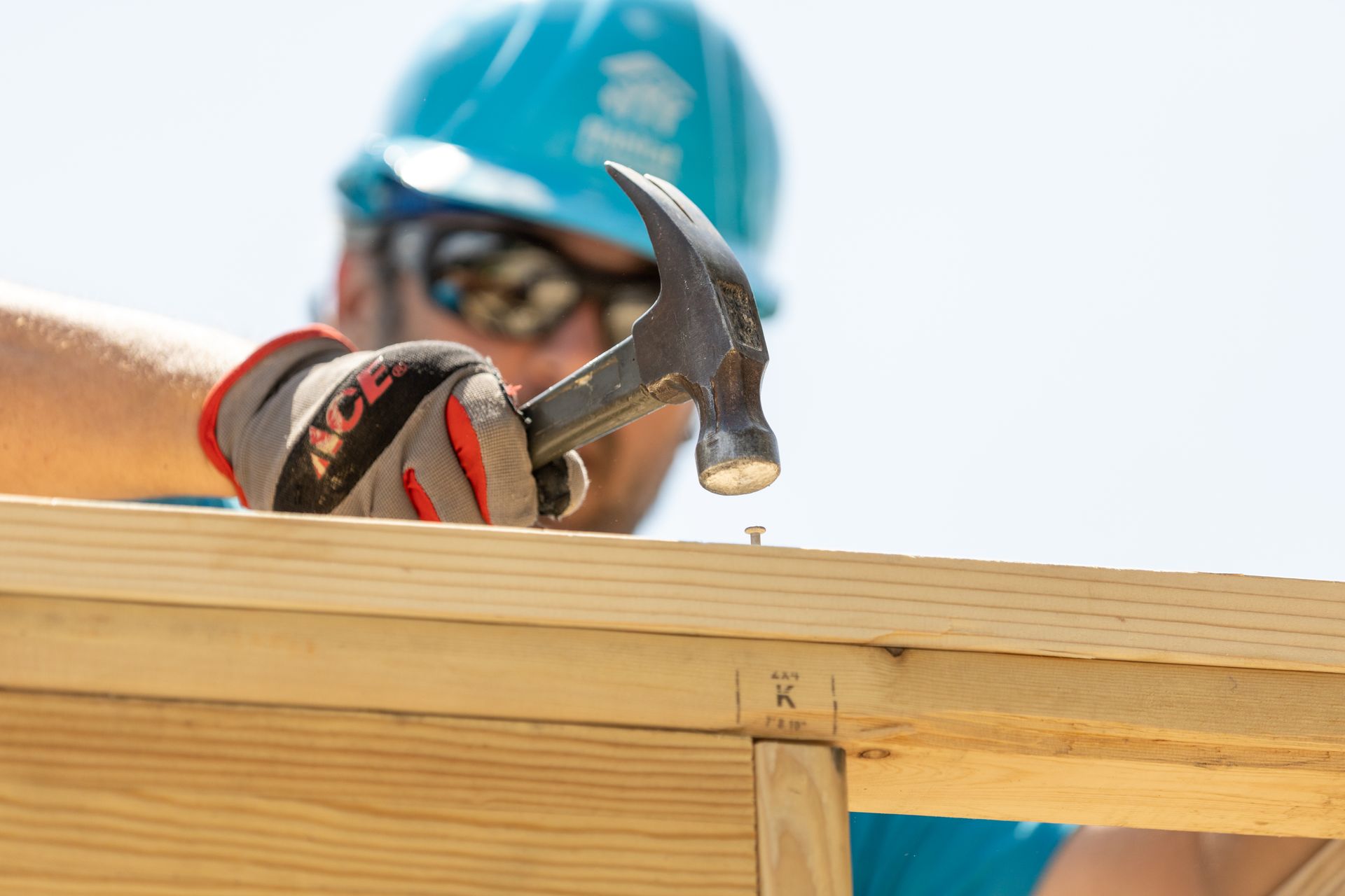 Habitat New Brunswick volunteer Construction worker hammering a wooden beam at a job site, wearing a blue hard hat and gloves