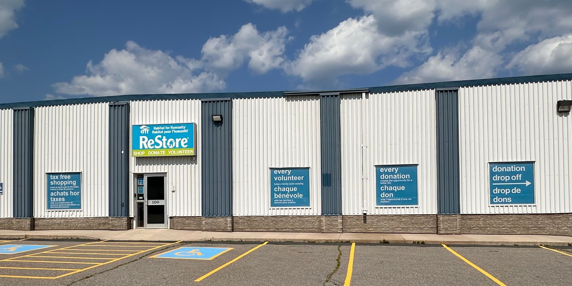 Restore Miramichi Exterior of a blue-and-white store with multiple blue signs and a central entrance under a cloudy sky