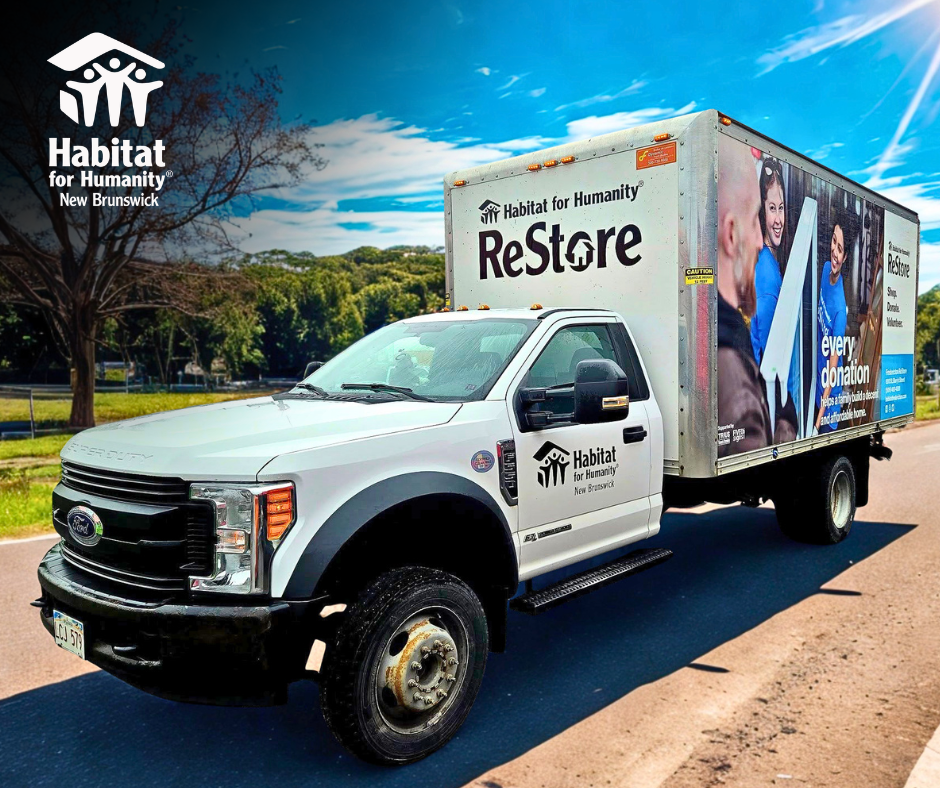Habitat for Humanity Restore truck parked on a sunny road, with a branded box trailer and home improvement ads.